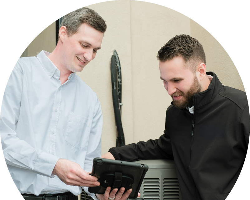 A Oosterveld technician in a white shirt shows service details on a tablet to a smiling client in a black jacket, standing beside an AC unit outside a beige building. A Oosterveld technician in a white shirt shows service details on a tablet to a smiling client in a black jacket, standing beside an AC unit outside a beige building.