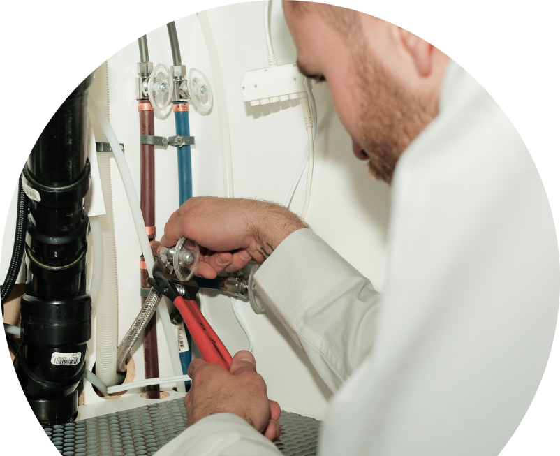 Oosterveld plumbing expert tightening connections under a sink during a faucet installation, surrounded by hot and cold water supply lines and PVC drainage. Oosterveld plumbing expert tightening connections under a sink during a faucet installation, surrounded by hot and cold water supply lines and PVC drainage.