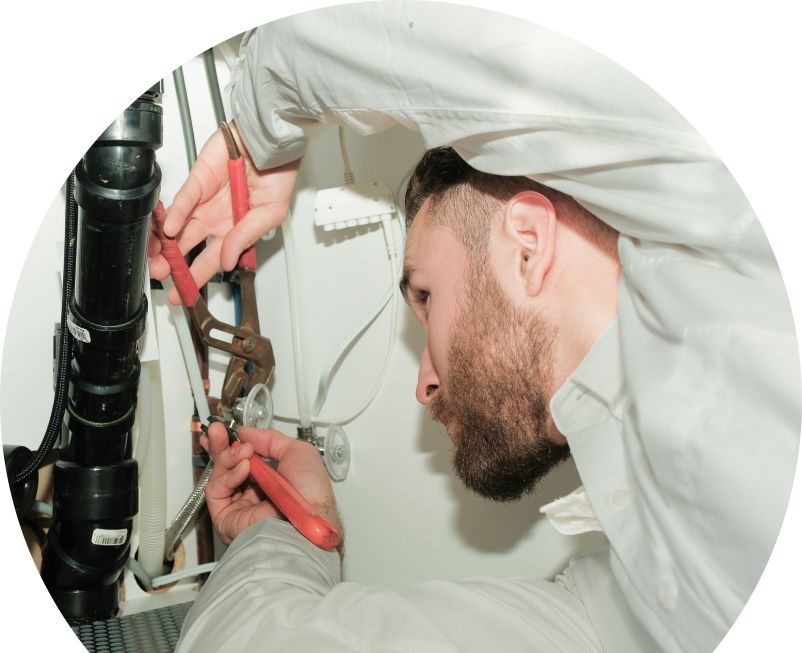 Oosterveld plumbing specialist uses hand tools to tighten pipe fittings beneath a sink during a repair, with visible wiring and drainage lines in the background.