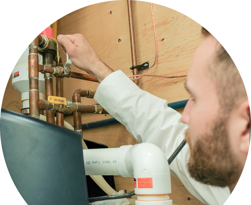 Oosterveld water heater specialist tightens a valve on copper piping during a water heater installation, with exposed wood paneling and wiring in the background. Oosterveld water heater specialist tightens a valve on copper piping during a water heater installation, with exposed wood paneling and wiring in the background.
