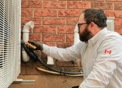 A Oosterveld HVAC specialist wearing glasses and gloves uses a diagnostic tool to service an outdoor AC unit beside a brick wall. A Oosterveld HVAC specialist wearing glasses and gloves uses a diagnostic tool to service an outdoor AC unit beside a brick wall.