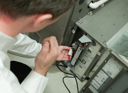 A Oosterveld heating technician inspecting internal wiring during a service check on a residential heating unit. A Oosterveld heating technician inspecting internal wiring during a service check on a residential heating unit.