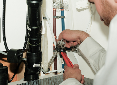 Using two pipe wrenches, a Oosterveld professional plumber services a pipe connection near a vertical flue or vent pipe. Using two pipe wrenches, a Oosterveld professional plumber services a pipe connection near a vertical flue or vent pipe.